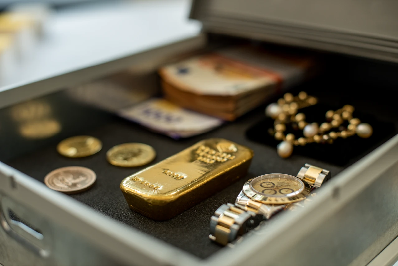 Geöffnetes Schließfach mit Goldbarren, Münzen, Bargeld, Schmuck und Armbanduhr.