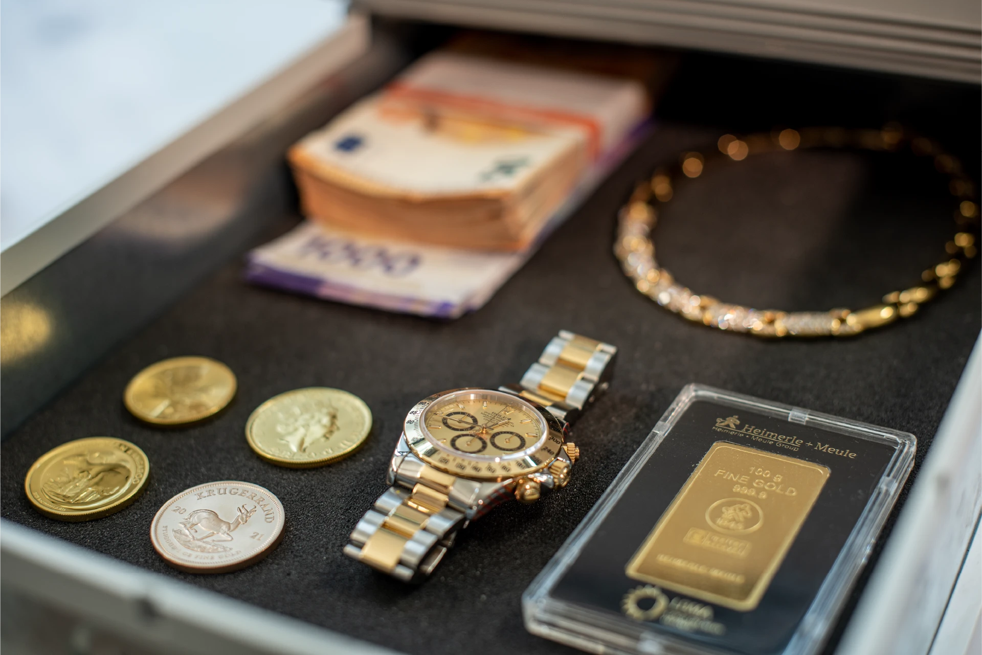 Geöffnetes Schließfach mit Luxusuhr, Goldbarren, Goldmünzen, Goldkette und Euroscheinen