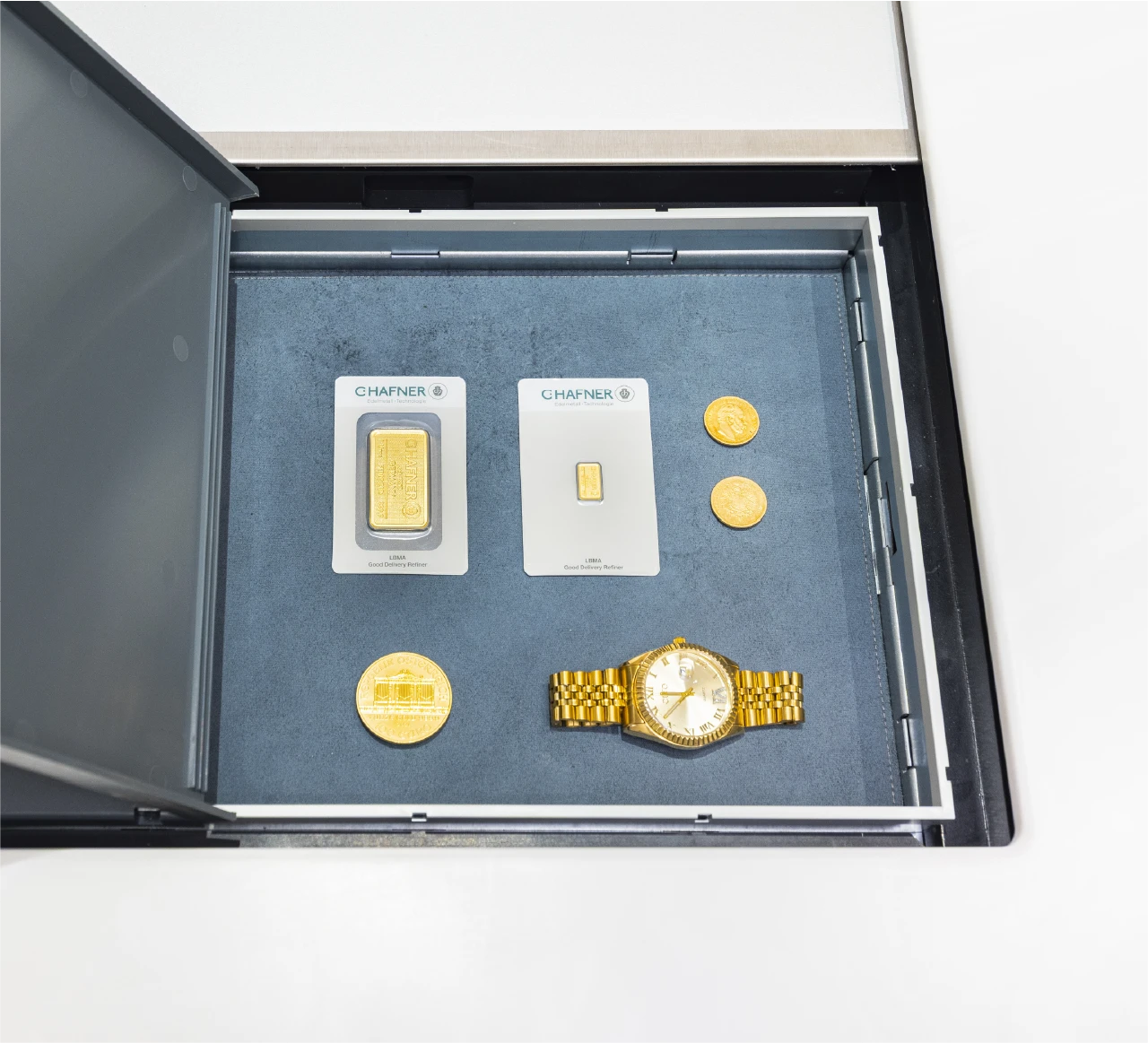 Geöffnetes Schließfach mit Goldbarren, Goldmünzen, zertifizierten Edelmetallen und einer Luxusuhr