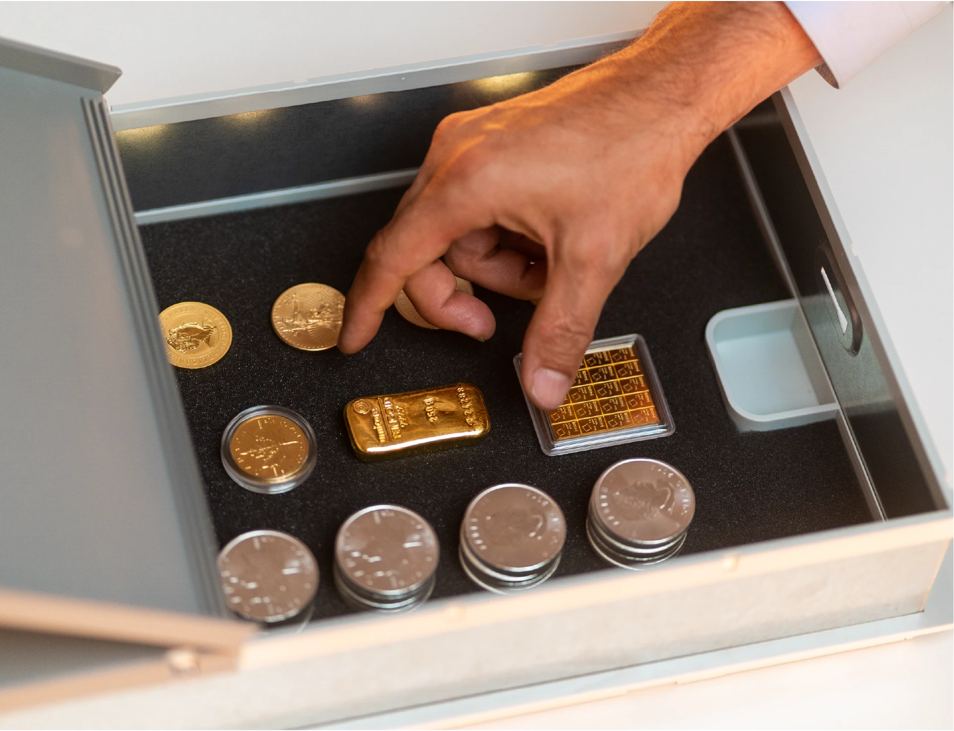 Open Trisor safe deposit box with gold bars and a hand retrieving precious metals