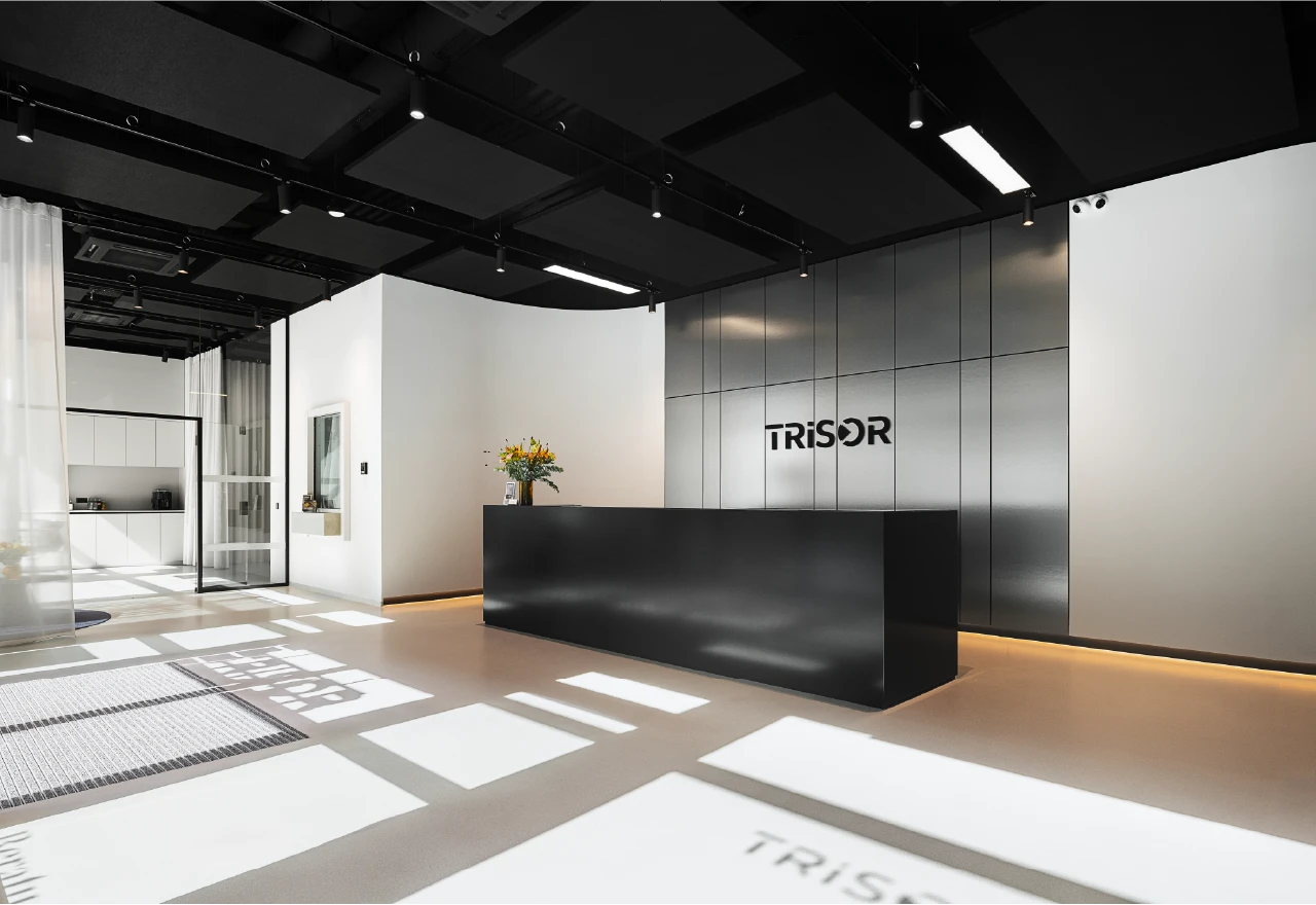 Eingangsbereich bei Trisor Stuttgart mit schwarzem Empfangstresen vor einer silbernen Metallwand mit Firmenlogo.