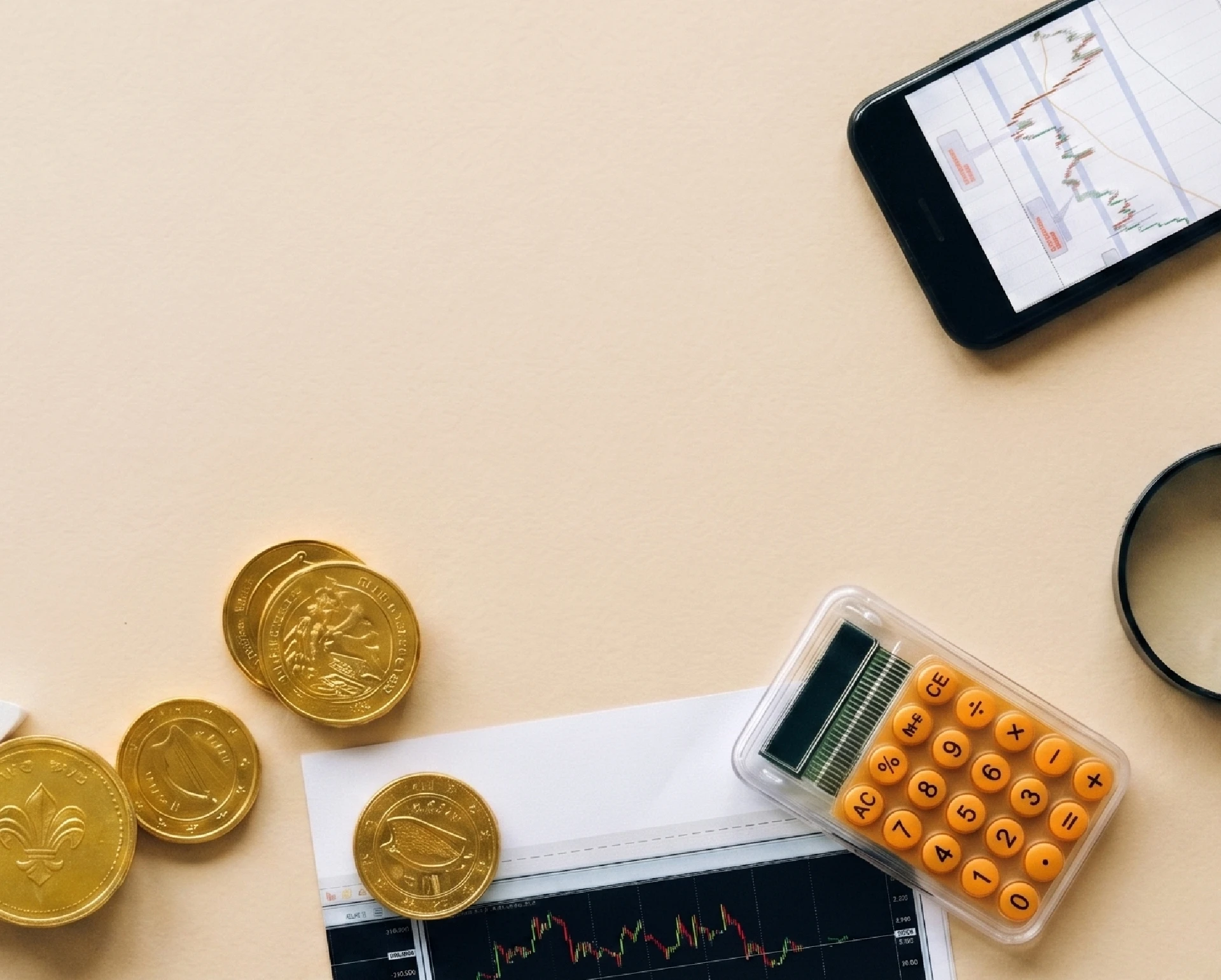 Goldmünzen, Taschenrechner, Börsenchart auf Papier und Smartphone mit Kursdiagramm auf beigem Untergrund