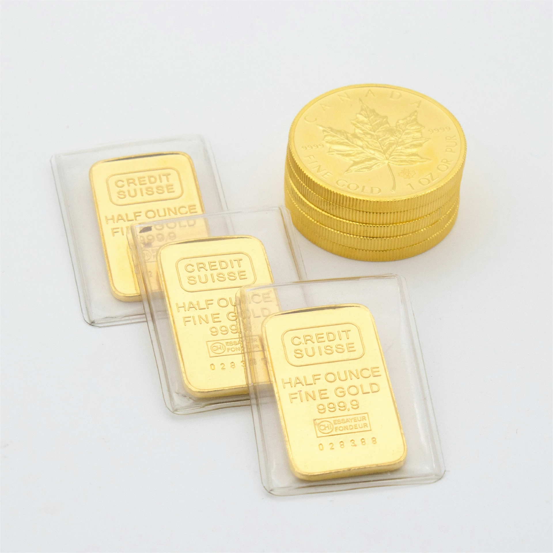 Drei Credit Suisse Goldbarren (Half Ounce, Feingold 999,9) in Kunststoffhüllen neben einem Stapel Goldmünzen