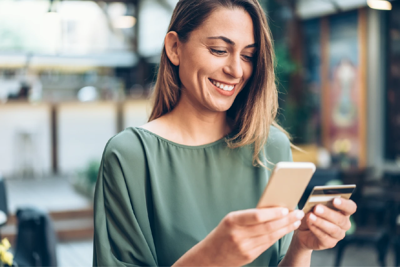 Smiling person holding a smartphone and a payment card in their hand.